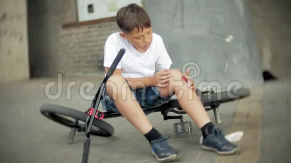 一个小男孩从自行车上摔下来后坐在公园里膝盖的疼痛得到缓解这是一辆危险的自行车视频的预览图