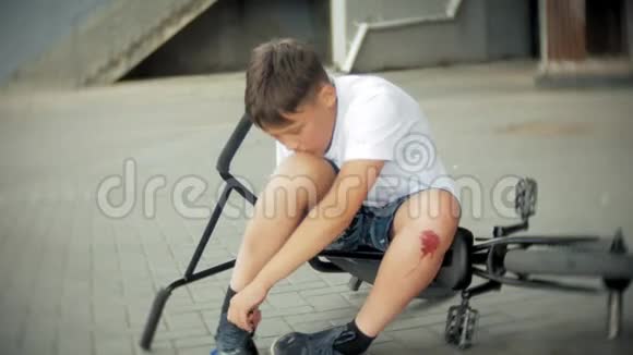 一个小男孩从自行车上摔下来后坐在公园里膝盖的疼痛得到缓解这是一辆危险的自行车视频的预览图