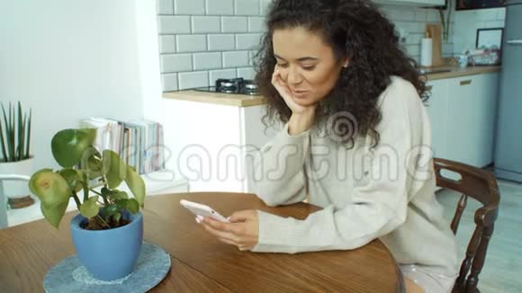 年轻的女人在厨房里用手机视频的预览图