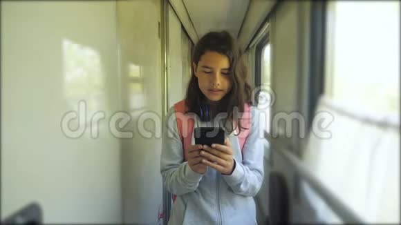 十几岁的女孩带着背包和智能手机在火车车厢里散步旅游运输铁路概念这就是视频的预览图