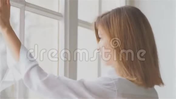 窗前漂亮的年轻女子穿着白色衬衫视频的预览图