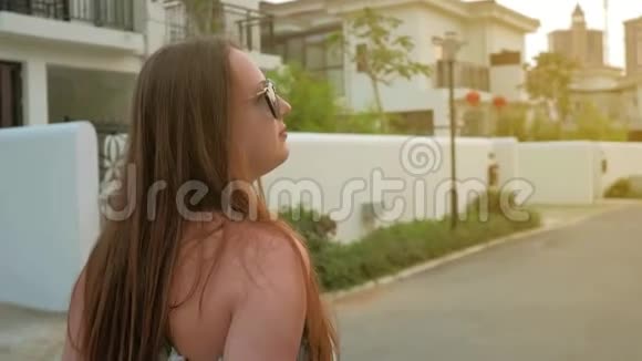 一个穿着蓝色连衣裙的年轻女孩正沿着热带城市的街道行走中弹慢动作视频的预览图