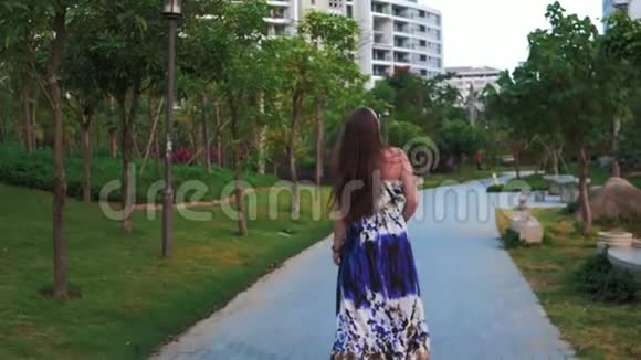 迷人的快乐女孩戴着眼镜和一件蓝色的裙子走在热带城市的街道上棕榈树和太阳视频的预览图