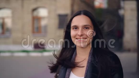 一幅美丽的年轻女子的慢镜头肖像看着相机微笑着站在户外与城市街道在视频的预览图