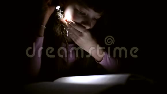 小女孩正在黑暗的房间里看一本带手电筒的书视频的预览图