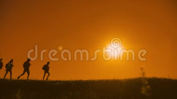 人们徒步旅行团和狗的轮廓阳光下的游客四个人走在夕阳的轮廓之上视频的预览图