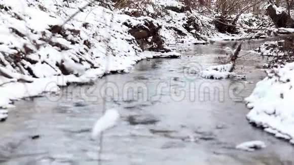 冰水在一条快速的泉水小溪里流淌水中岩石上的雪视频的预览图