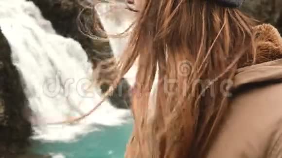 近距离观看年轻女子站在冰岛一个强大的瀑布附近头发随风飘扬视频的预览图