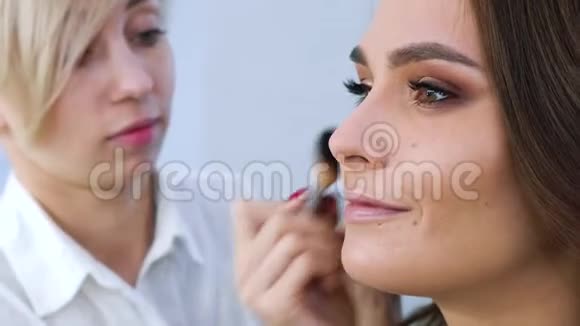 化妆师将化妆品应用于年轻女性面部特写视频的预览图
