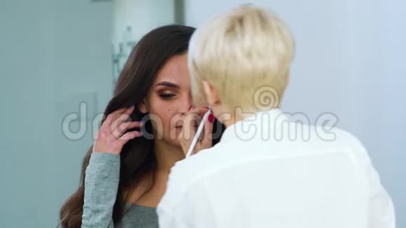 化妆师在年轻女子脸上涂化妆品视频的预览图