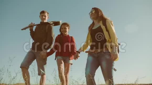 快乐家庭慢动作视频行走在大自然男孩女孩和妈妈在野外徒步旅行带吉他的游客视频的预览图