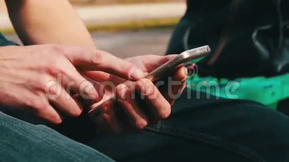 带着白色电话的年轻人坐在春天的街道上公园里户外视频的预览图