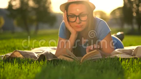 戴眼镜的女孩在日落时躺在公园的毯子上看书视频的预览图