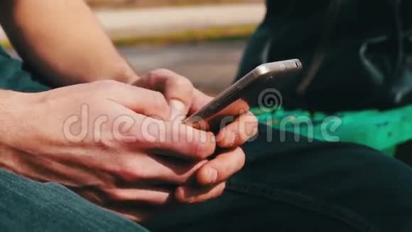 带着白色电话的年轻人坐在春天的街道上公园里户外视频的预览图