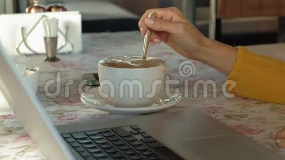 年轻女子带着现代笔记本电脑坐在咖啡馆里喝着咖啡卡布奇诺视频的预览图