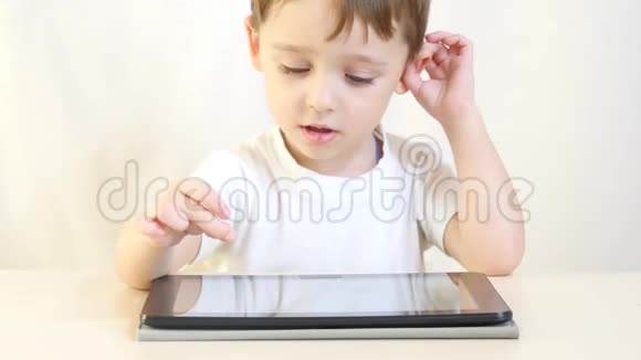 孩子正坐在桌子旁在平板电脑上玩视频的预览图