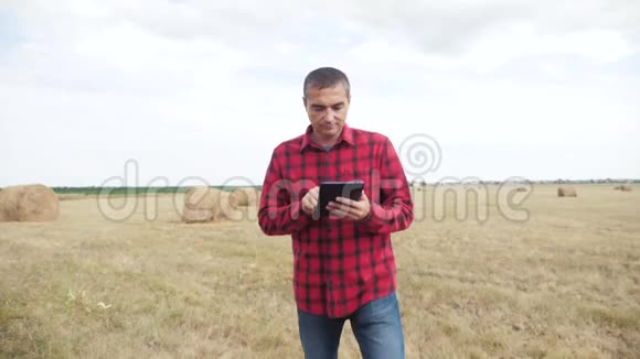 智慧农业生活方式理念农夫在数字平板电脑上的田野里研究干草堆慢动作视频的预览图