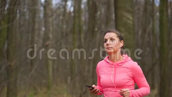 日落时分一位戴着耳机和智能手机的女士穿过一片秋林视频的预览图