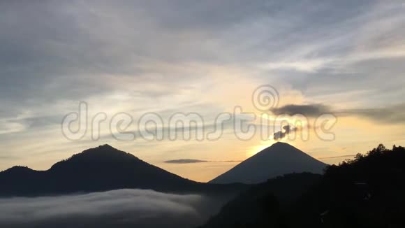巴图尔湖上空的日出覆盖着云彩和阿贡火山喷发的烟雾从巴图尔山顶部看到在巴厘岛印度尼西亚视频的预览图