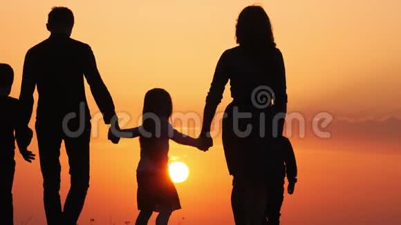 日落时幸福家庭的剪影一起在草地上散步视频的预览图