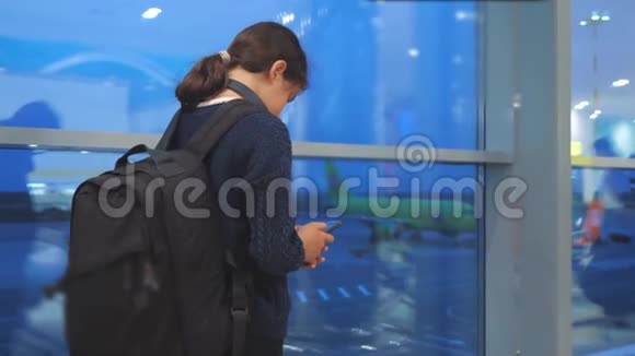 女儿旅行者带背包飞机航班机场概念带着智能手机的少女望着窗外视频的预览图