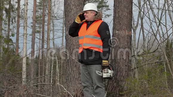 戴着电锯的伐木工人在树旁用智能手机聊天视频的预览图