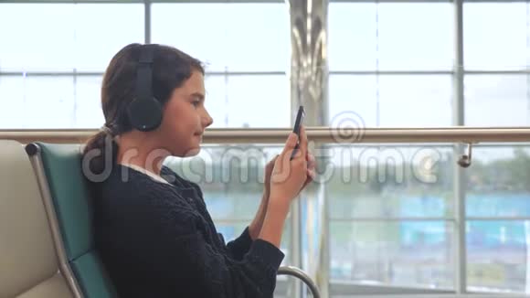 机场候机大厅的生活方式一架飞机戴着耳机听音乐的年轻快乐少女视频的预览图