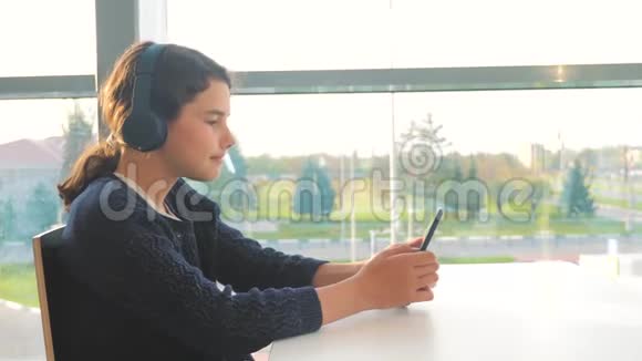 年轻快乐的少女戴着耳机听着音乐在智能手机上聊天在信使中交流视频的预览图