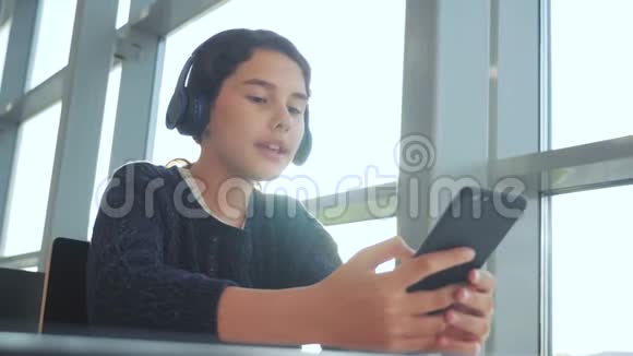年轻快乐的少女戴着耳机听着音乐在智能手机上聊天在信使中交流视频的预览图