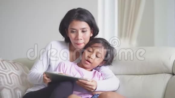 小女孩和妈妈在沙发上用平板电脑视频的预览图