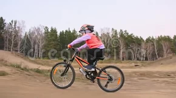 一个高加索儿童在土公园骑自行车道在赛马场骑黑色橙色自行车的女孩孩子是干的视频的预览图
