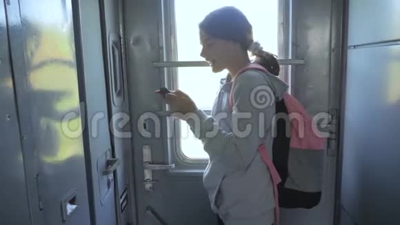 年轻的女孩旅行者带着背包站在火车的窗户边有一个生活方式的智能手机旅费视频的预览图