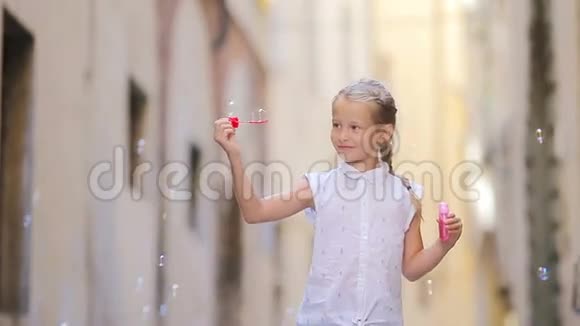 可爱的小女孩户外吹肥皂泡在欧洲城市白种人儿童享受暑假的肖像视频的预览图