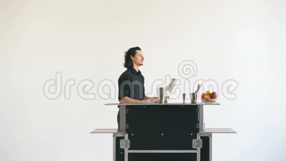 教授调酒师男子在白色背景工作室的移动酒吧桌上摆弄瓶子和摇鸡尾酒视频的预览图