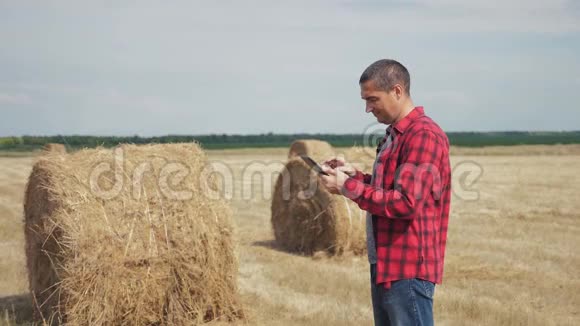 智慧农耕生活方式农业理念一名农民工人在数字平板电脑上的田野里研究干草堆慢慢慢慢视频的预览图