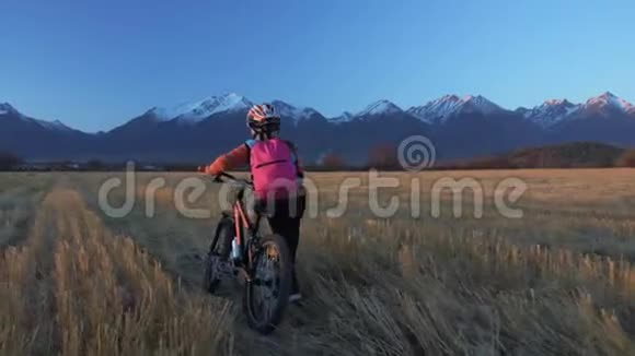 一个高加索儿童骑着自行车在麦田里行走女孩在美丽的白雪公主的背景下走着黑色橙色的自行车视频的预览图