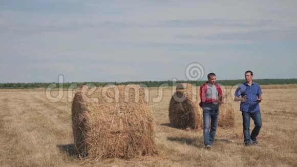 生活方式团队合作农业智慧养殖理念两个男的农民工人走在田野的干草堆上视频的预览图
