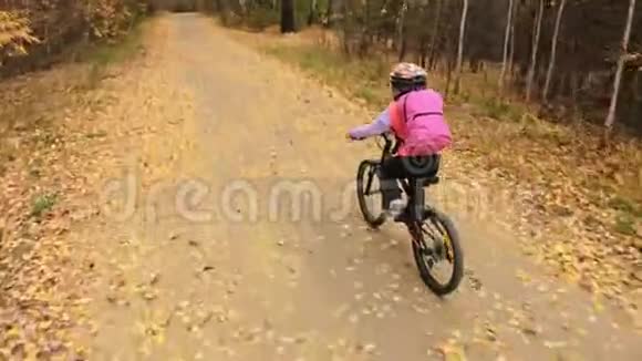 一个高加索儿童在秋季公园骑自行车小女孩骑着黑色橙色的自行车在森林里孩子是干的视频的预览图