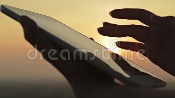 日落时分手持数码平板电脑的女人视频的预览图