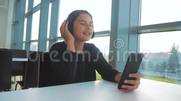 快乐的年轻少女戴着耳机唱歌听着智能手机上的音乐社交网络中的少女视频的预览图