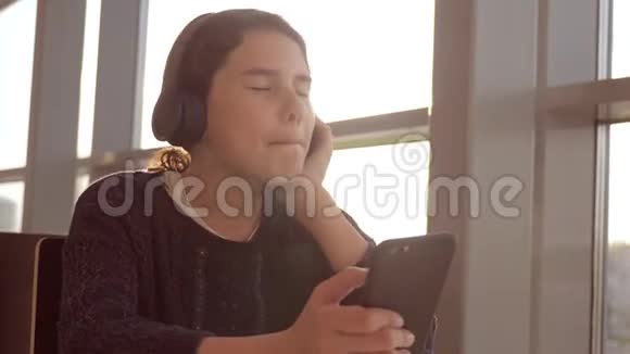 戴着耳机的快乐年轻少女在生活方式智能手机上唱歌和听音乐社交界的少女视频的预览图