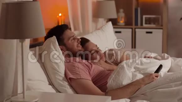 幸福的一对夫妇晚上在床上看电视视频的预览图