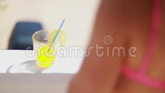 年轻女子穿着泳衣在夏季露台上喝着黄色柠檬饮料视频的预览图
