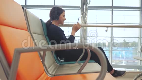 机场候机大厅供飞机飞行年轻的生活方式快乐的少女耳机听音乐视频的预览图