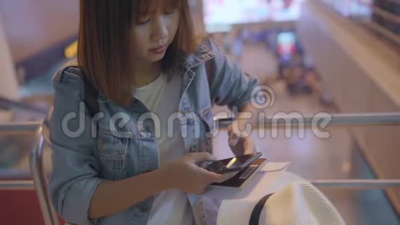 快乐的亚洲女人在机场登机口等待航班时在候机大厅使用和检查她的智能手机视频的预览图