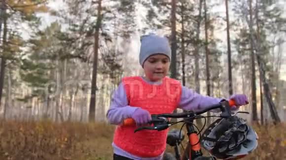 一个高加索儿童在秋天公园骑自行车走路小女孩在森林里走着黑色的橙色循环孩子是干的视频的预览图