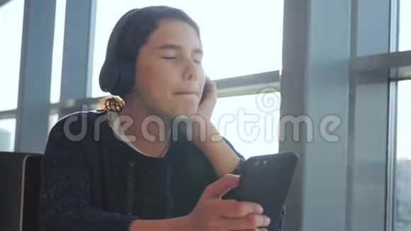 戴着耳机的快乐年轻少女在智能手机生活方式上唱歌和听音乐少年女孩视频的预览图