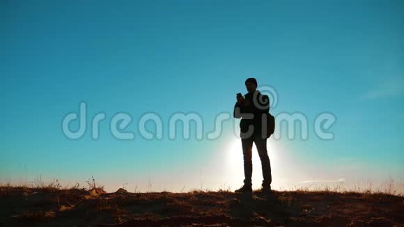 男子值得旅游与背包智能手机导航阳光站在山顶慢速视频视频的预览图
