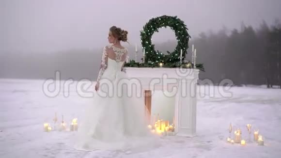 冰湖边壁炉装饰处穿白色连衣裙的年轻女子视频的预览图