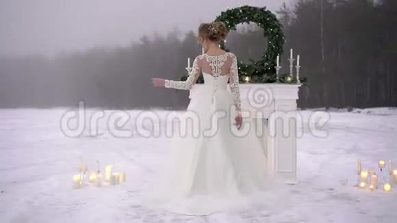 冰湖边壁炉装饰处穿白色连衣裙的年轻女子视频的预览图